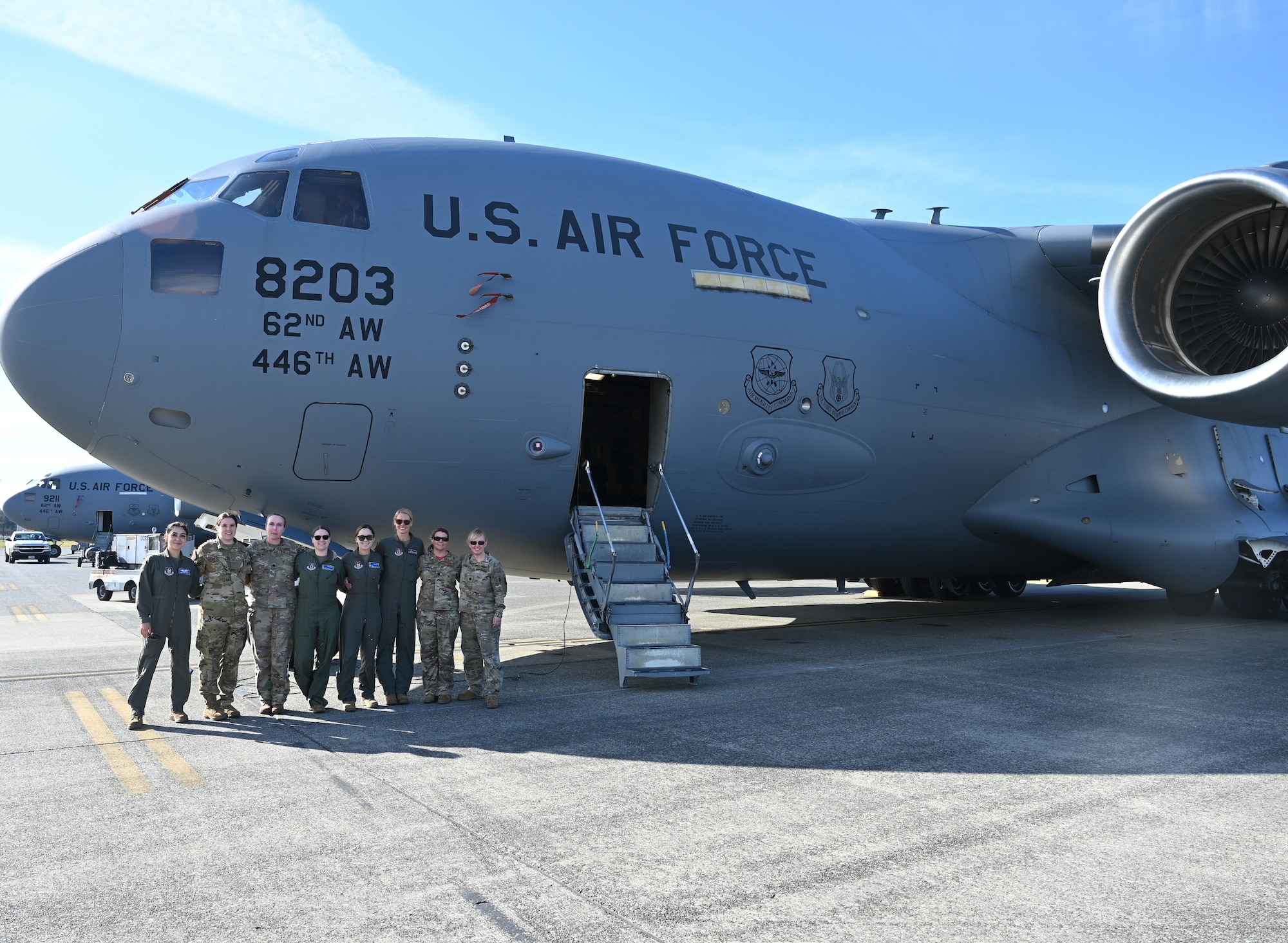 A group of eight women pose for a photo on the runway in front of a C-17 Globemaster.