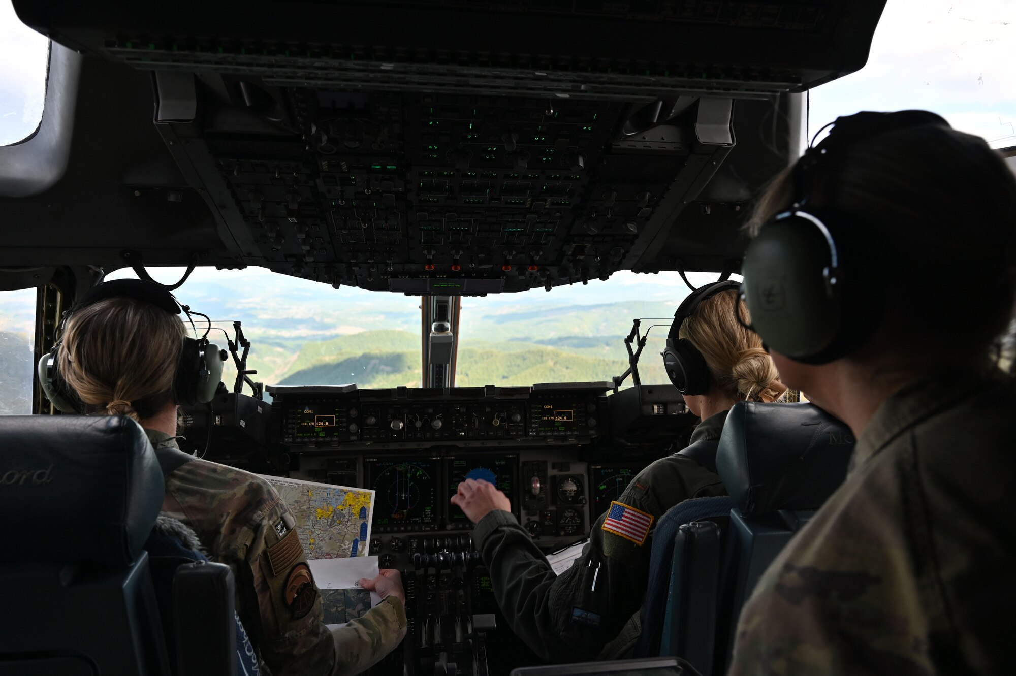 Two female pilots fly a C-17 over green rolling hills.