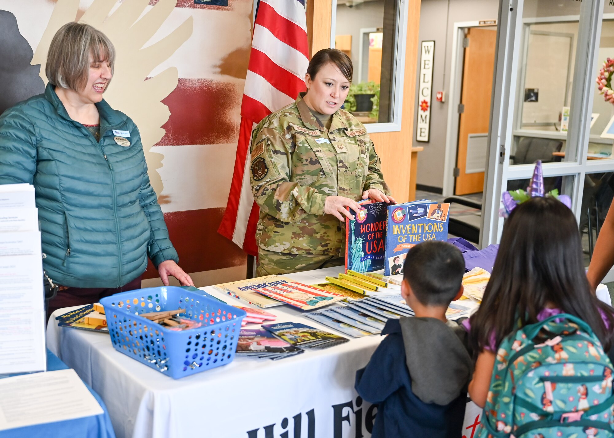 Lisa Hymas, military and family life counselor, and Tech. Sgt. Alicia Ringlehan, both with the Hill Air Force Base Military and Family Readiness Center, hand out books to students