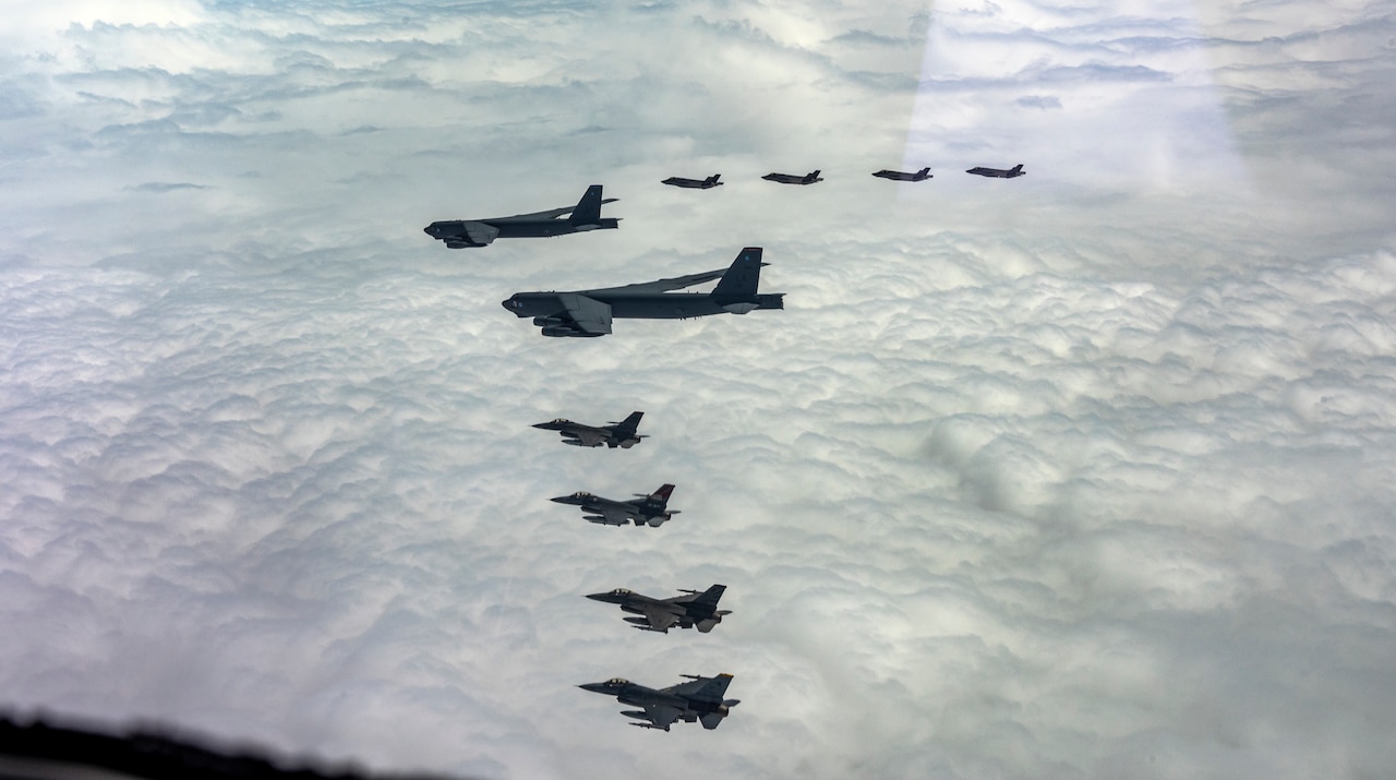 A group of military aircraft fly above clouds in formation.