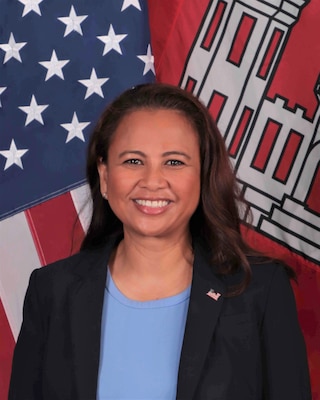 Official photo of Ms. Regina Jugueta-Vetter, Pacific Ocean Division Chief of Staff. Ms. Jugueta-Vetter is smiling, posing in front of the National and USACE Colors. She is wearing a blue shirt and dark blue blazer with a U.S. flag pin on the upper left chest.