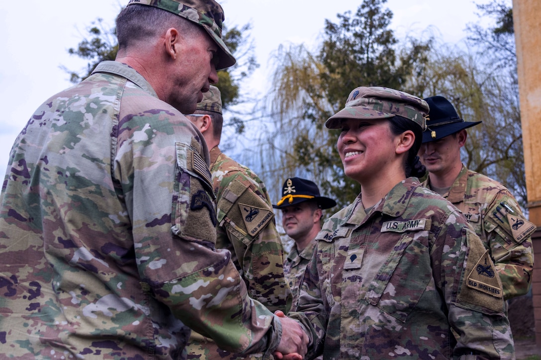 A senior officer shakes hands with a service member as she smiles.