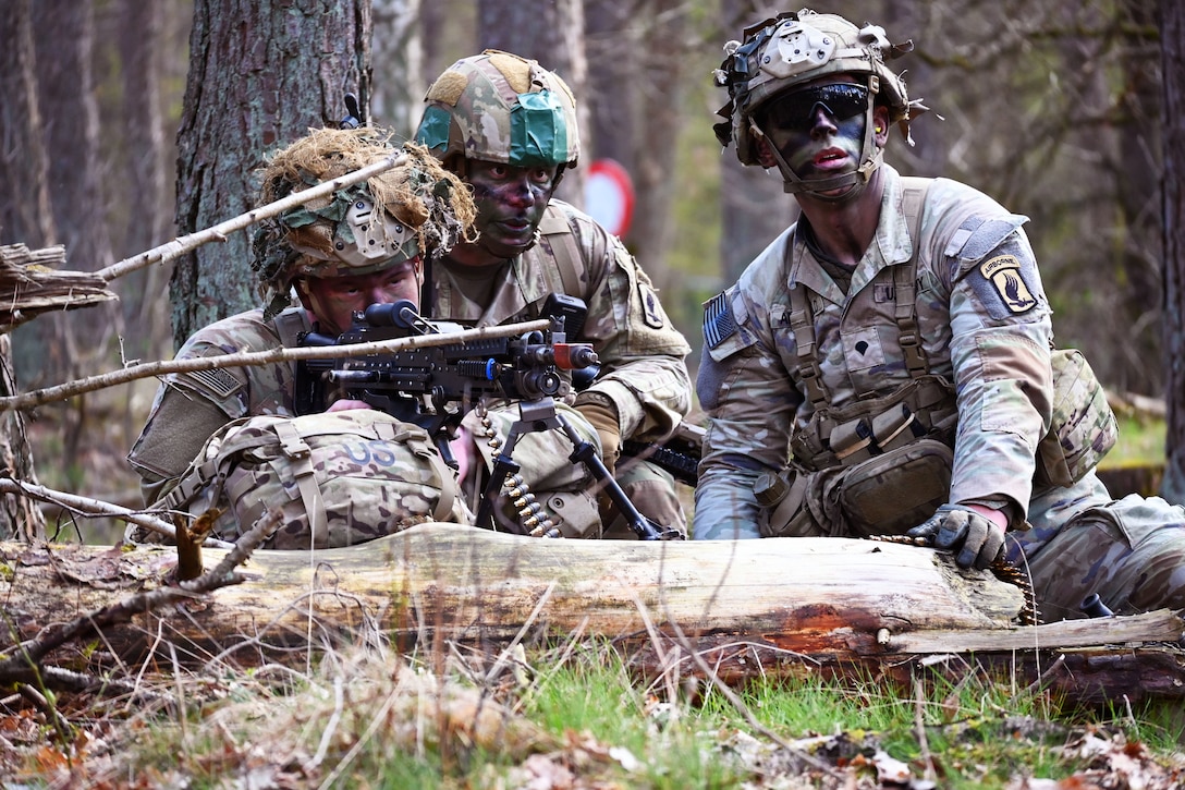 One soldier holds a weapon while two other soldiers look on.