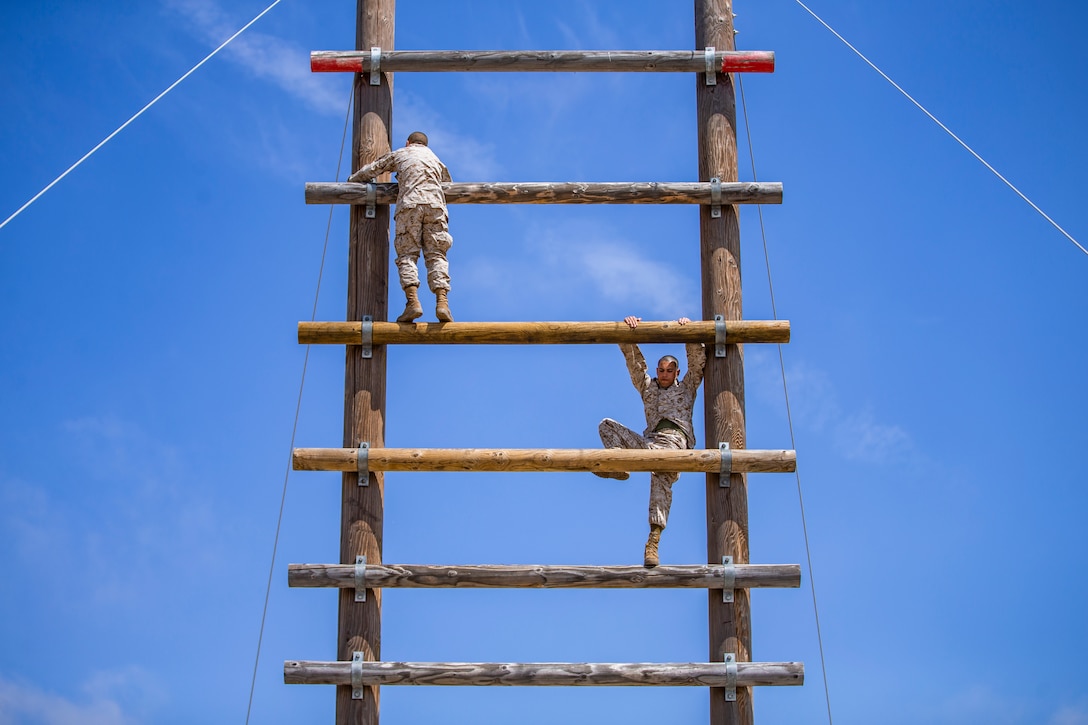 Marine Corps recruits climb a large ladder.