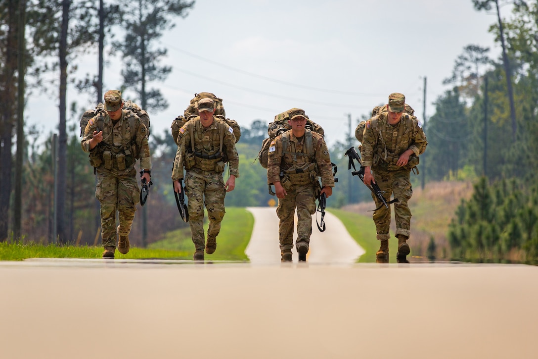 Four soldiers carry weapons as they walk beside each other along a road.