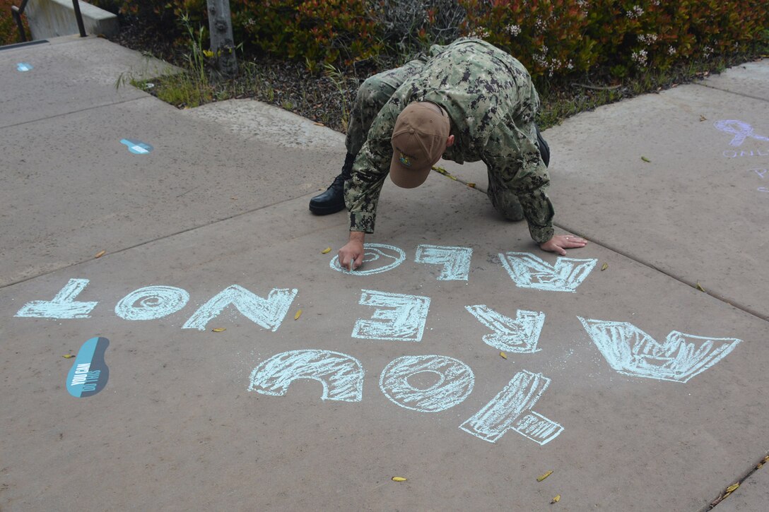 Sailor writes a message in chalk on the sidewalk.