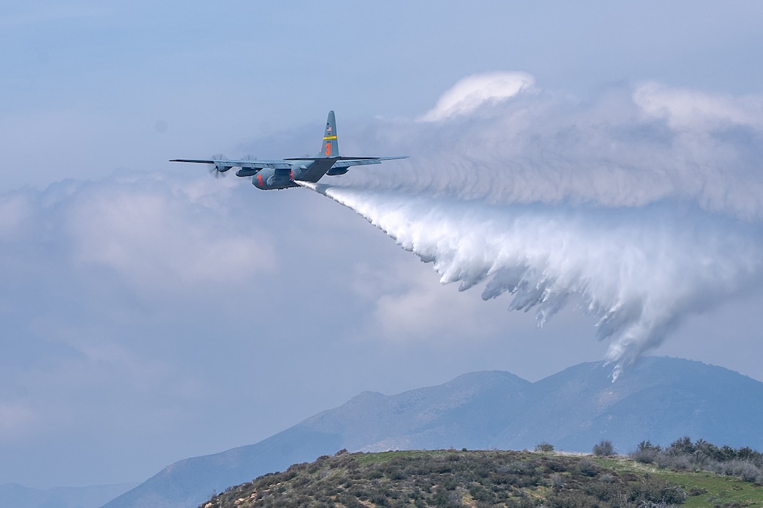 A military aircraft drops water over a mountainous area.