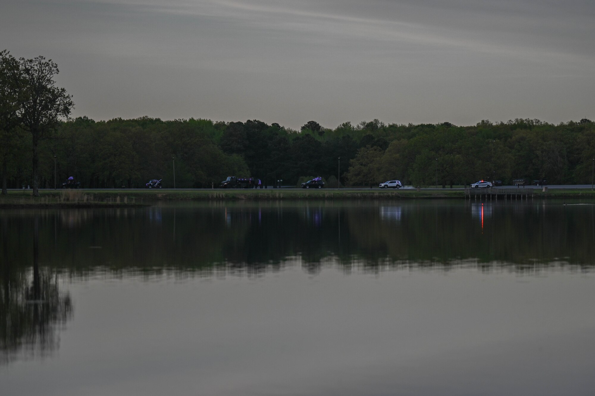 A line of vehicles drive along a lake.