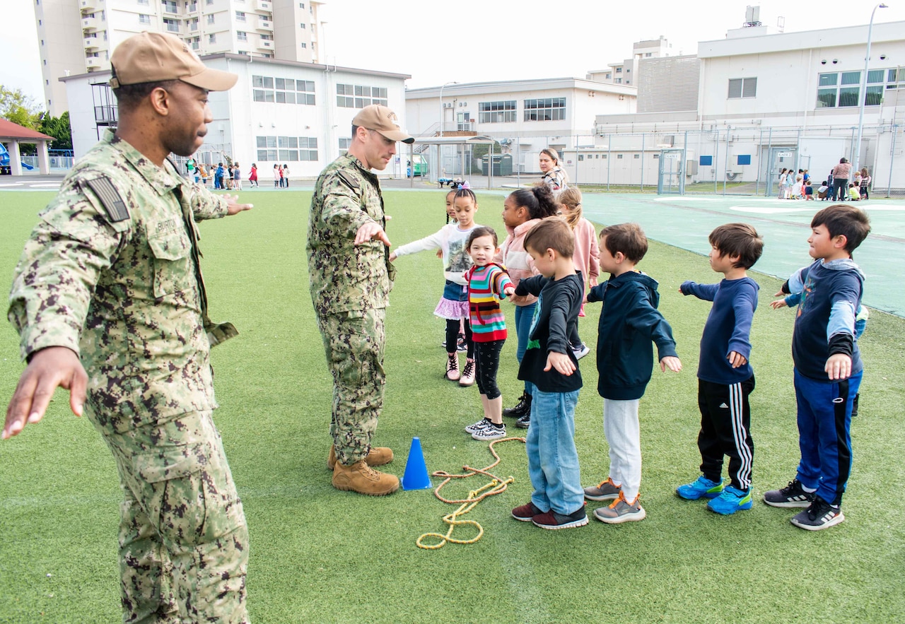 Sailors give instructions to students standing on a field.