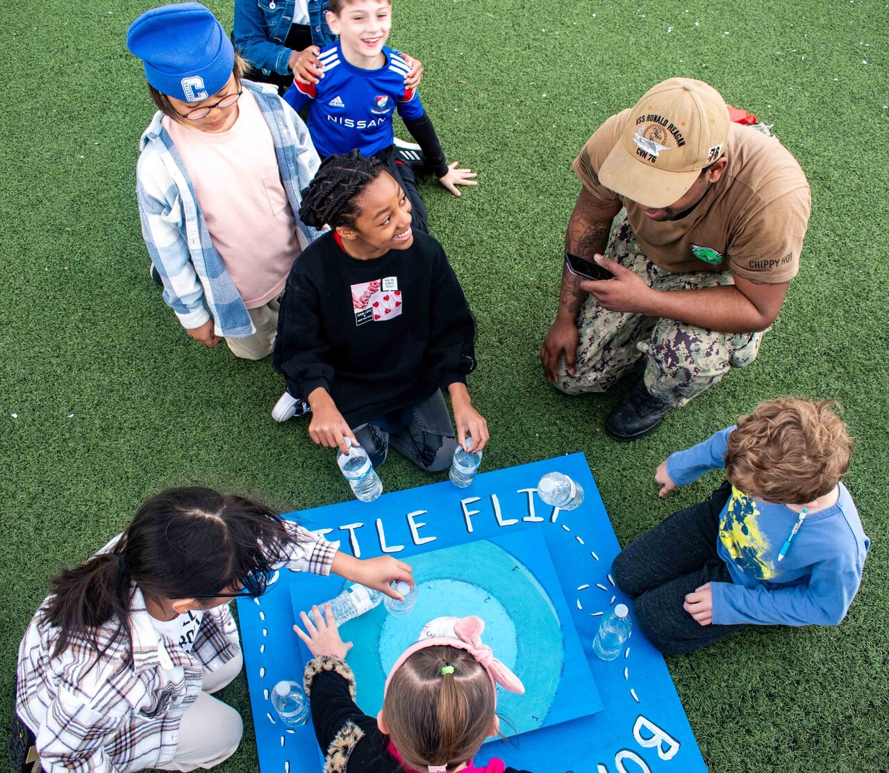 A sailor teaches students how to play bottle flipping game.