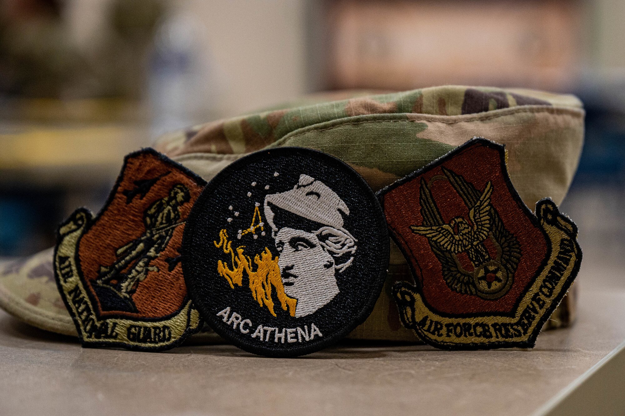 Three military patches sit propped against an OCP hat