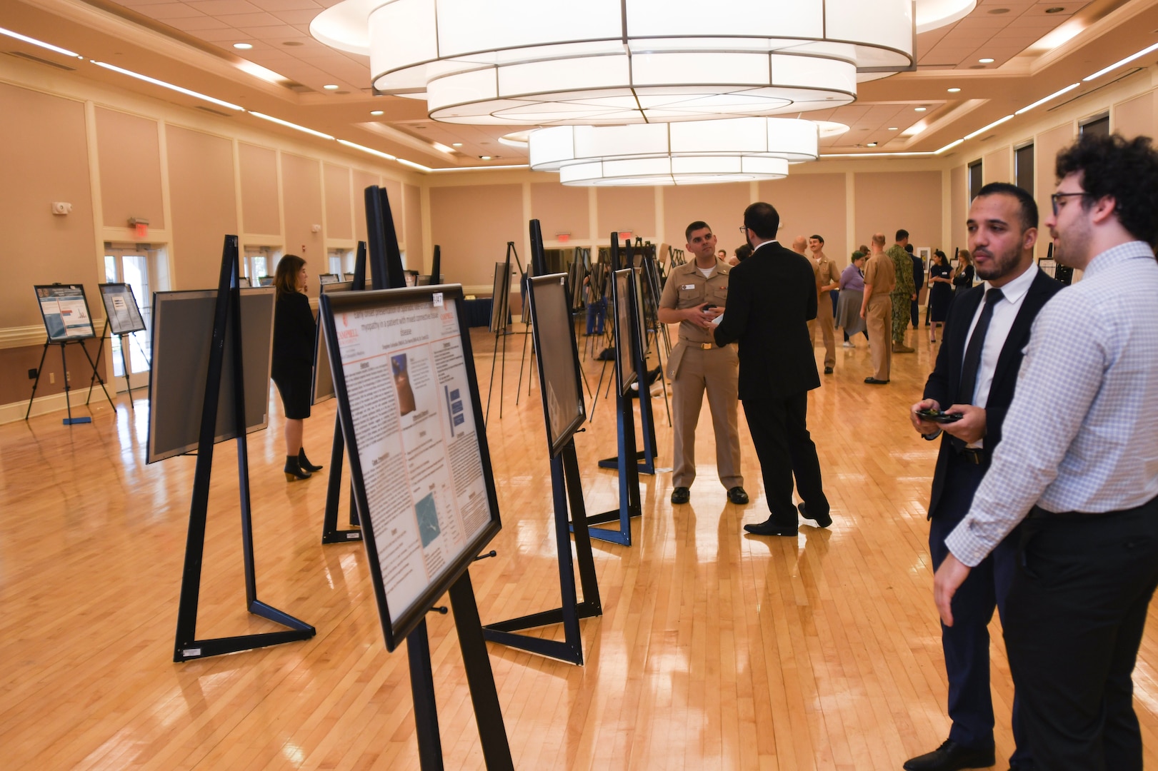 A participant in Naval Medical Center Camp Lejeune's 13th Annual Research Symposium meets with judges to discuss the research behind the poster presentation for their research. This year's symposium featured 73 submissions from NMCCL, 2nd Medical Battalion, 2nd Dental Battalion, Marine Raider Battalion, Campbell University, Duke University and Cape Fear Valley Health. Research submissions included poster and podium presentations with awards presented in various categories.