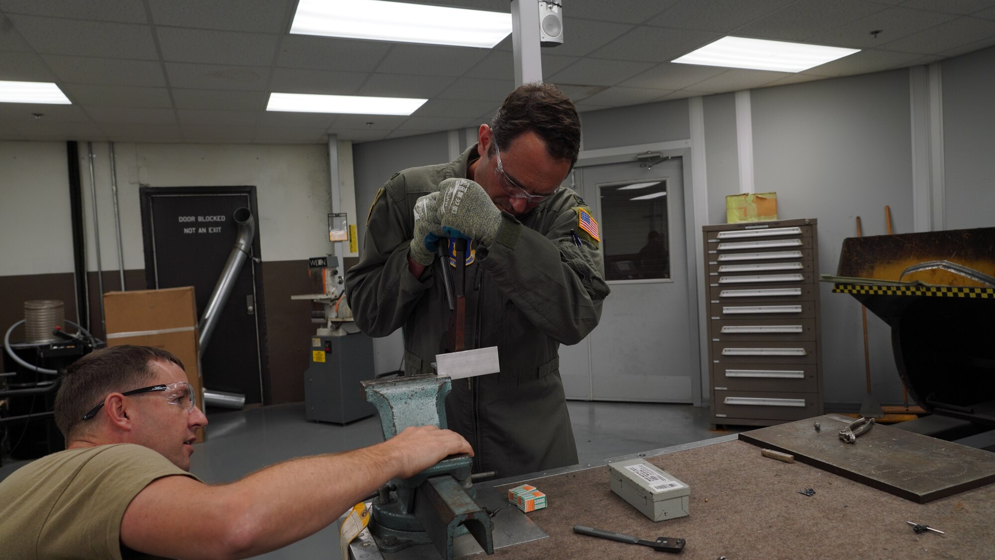 Master Sgt. explains how to use the solid rivets and hand rivet squeezers, then observes the vice commander perform the task.