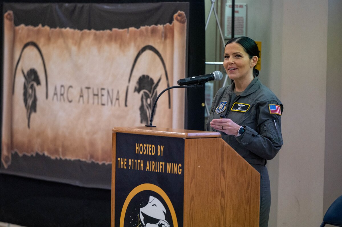 Senior Master Sgt. Rebecca Schatzman stands at a podium with a banner reading "ARC Athena" in the background
