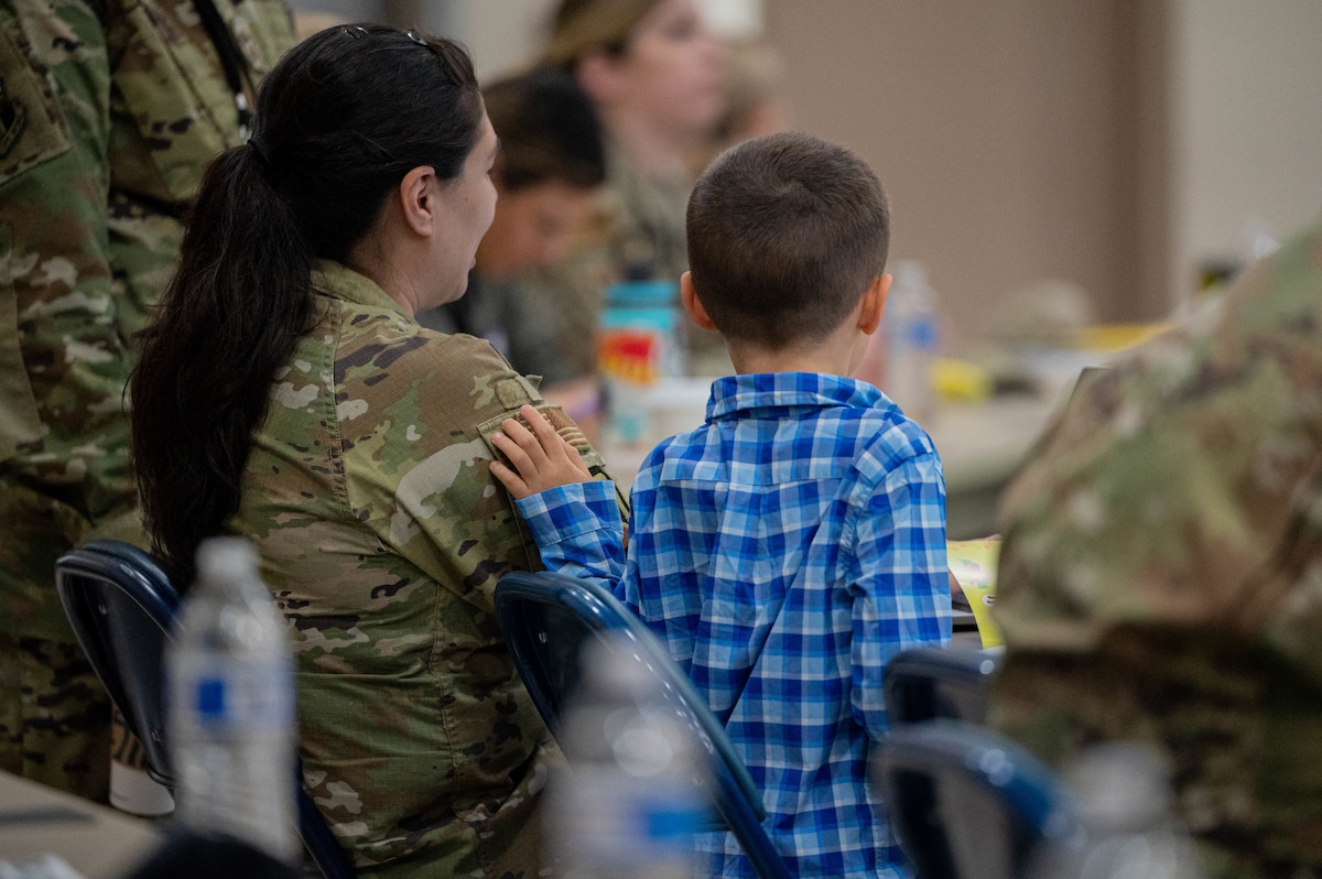 An Airman and their child sit with their backs to the camera