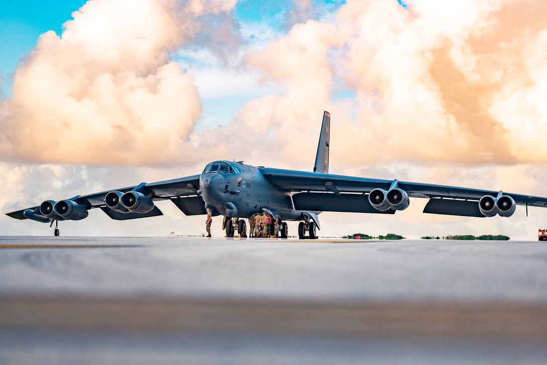 Service members stand together and inspect the underside of a large bomber.