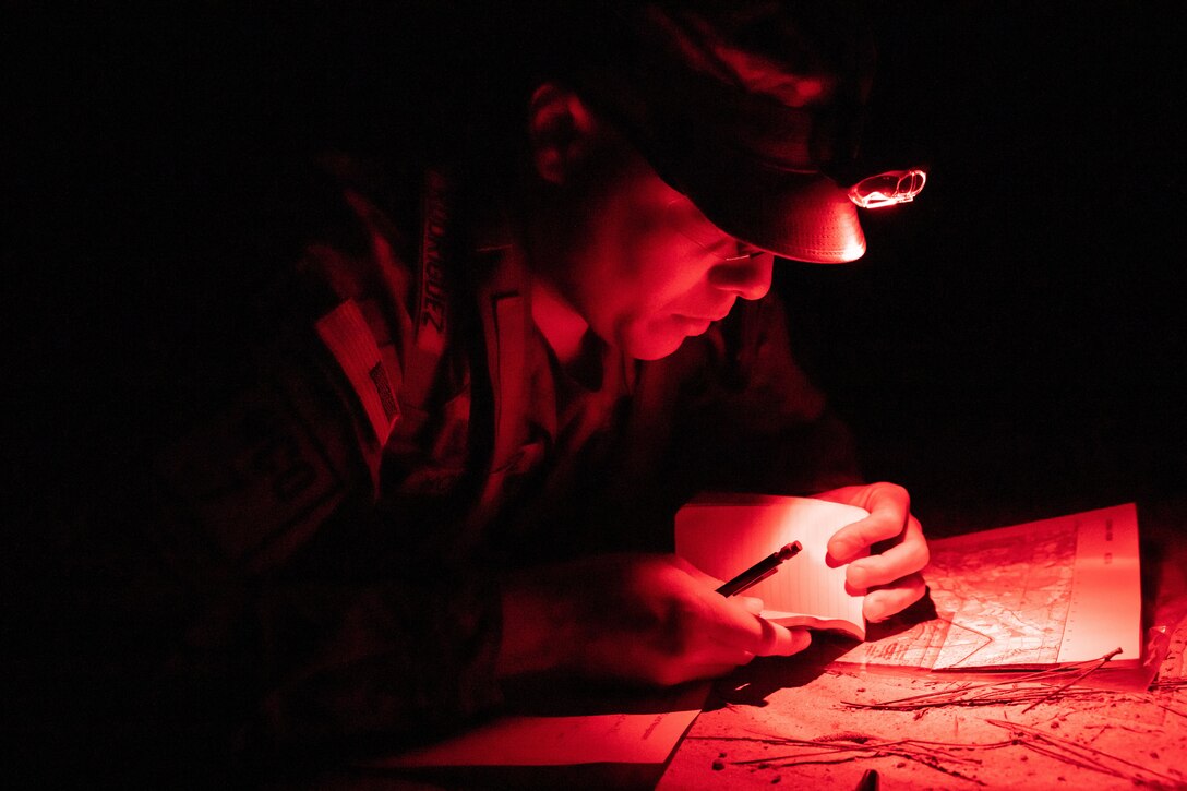 A soldier looks through a small notebook in the dark.