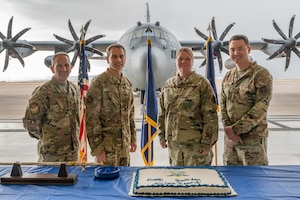 Four individuals prepare to cut a cake, while standing in front of a C-130J Super Hercules.