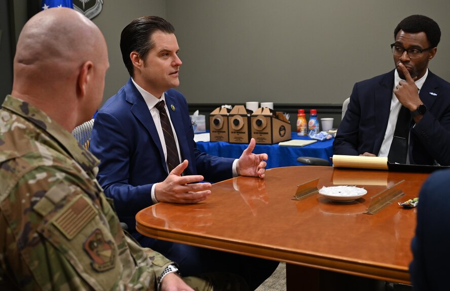 A congressman, a military legislative assistant, and military commander sit at a conference table.