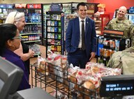 Congressman stands in a shoppette surrounded by food items and talks to military members and shoppette employees.