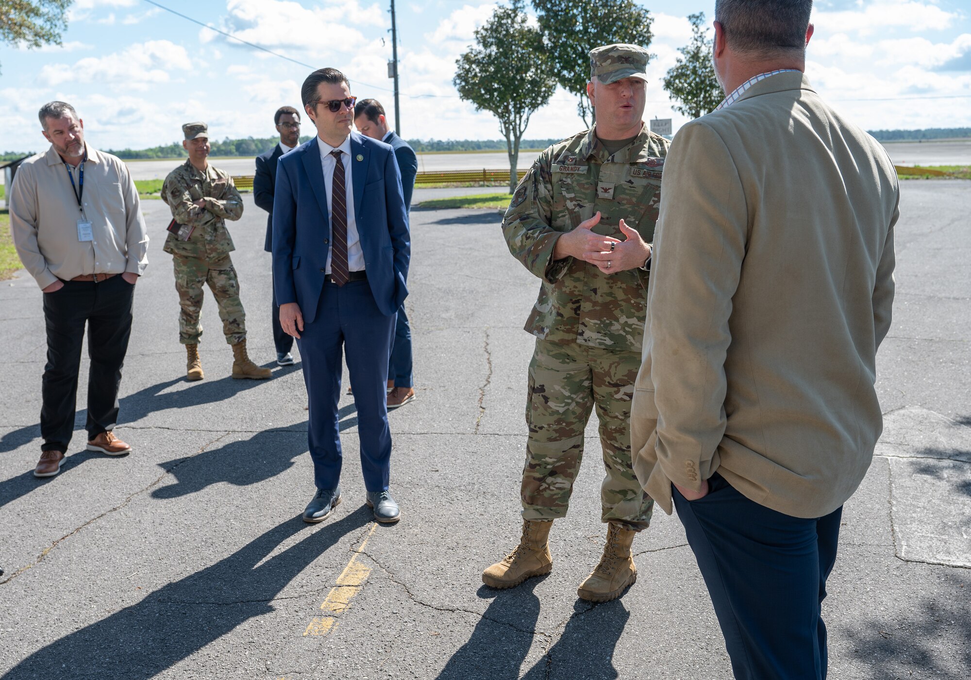 An Air Force military commander, congressman and other senior leadership stand outside in front of a flightline.