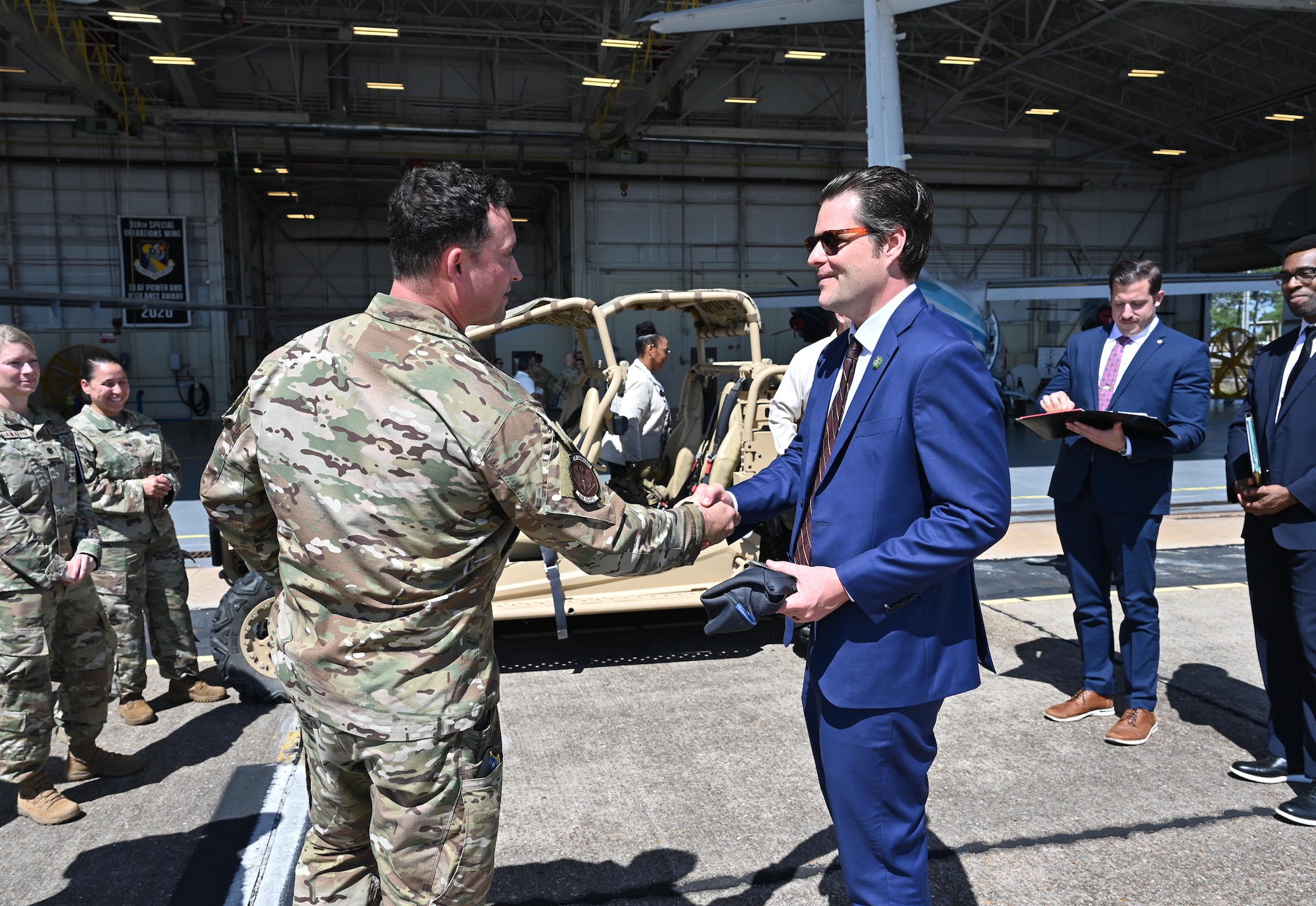 Congressman and Airman shake hands in front of an all-terrain vehicle parked in front of a C-146A Wolfhound hangar