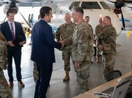 Congressman and military member shake hands in a hangar. Other senior leadership stand around with C-146A aircraft behind them.