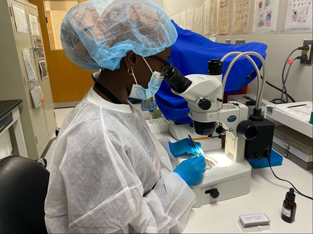 Young woman works at lab bench dressed in PPE.