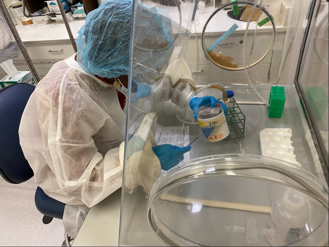 Young woman works at lab bench dressed in PPE.