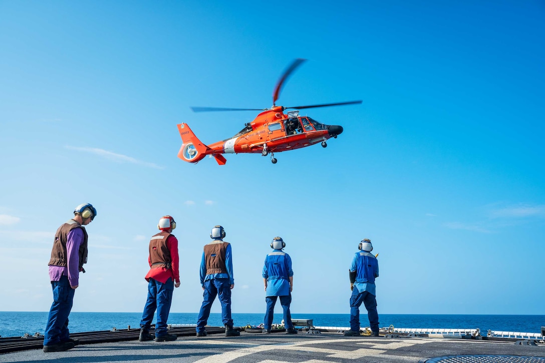 Tie-down crew aboard the U.S. Coast Guard Cutter Active (WMEC 618) prepare to deploy a fuel hose to an Airbus MH-65 helicopter in the Eastern Pacific Ocean, March 17, 2023. Active performed an in-flight refueling exercise, in which the helicopter hovers over the deck and receives fuel from the ship. (U.S. Coast Guard photo by Petty Officer 2nd Class Justin Upshaw).