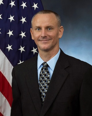 Official portrait of a man sitting in front of the American flag.