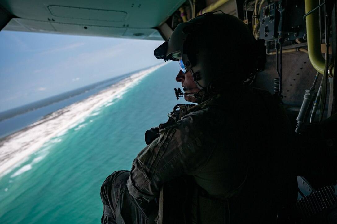 An airman looks out over the ocean from an aircraft.