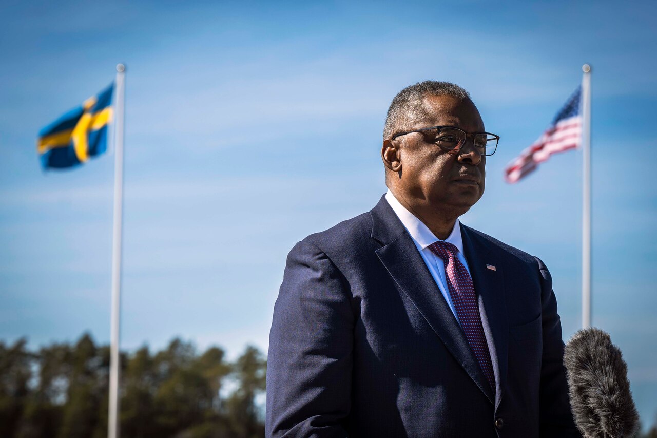 Defense Secretary Lloyd J. Austin III stands between the U.S. and Swedish flags.