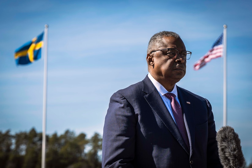 Defense Secretary Lloyd J. Austin III stands between the U.S. and Swedish flags.