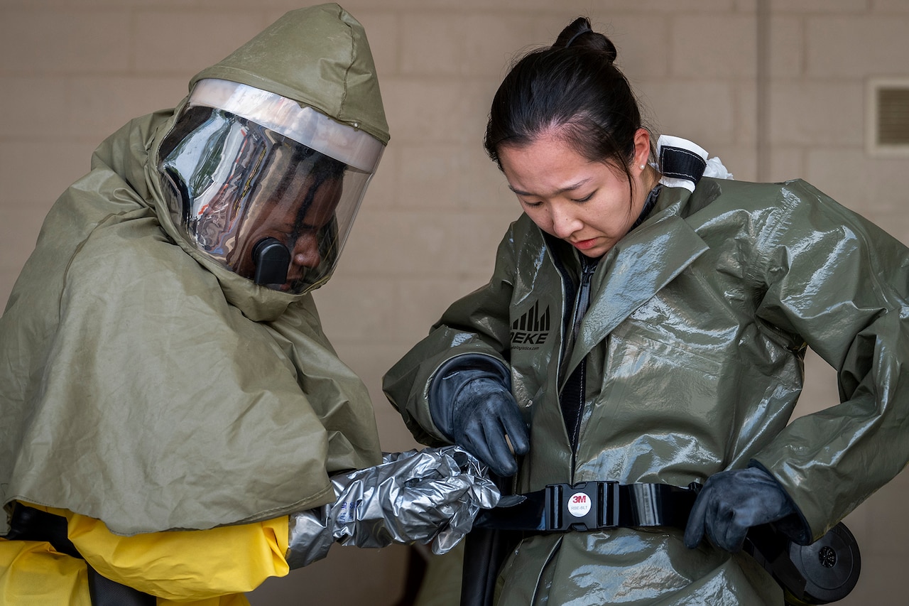 An airmen helps another adjust protective gear.