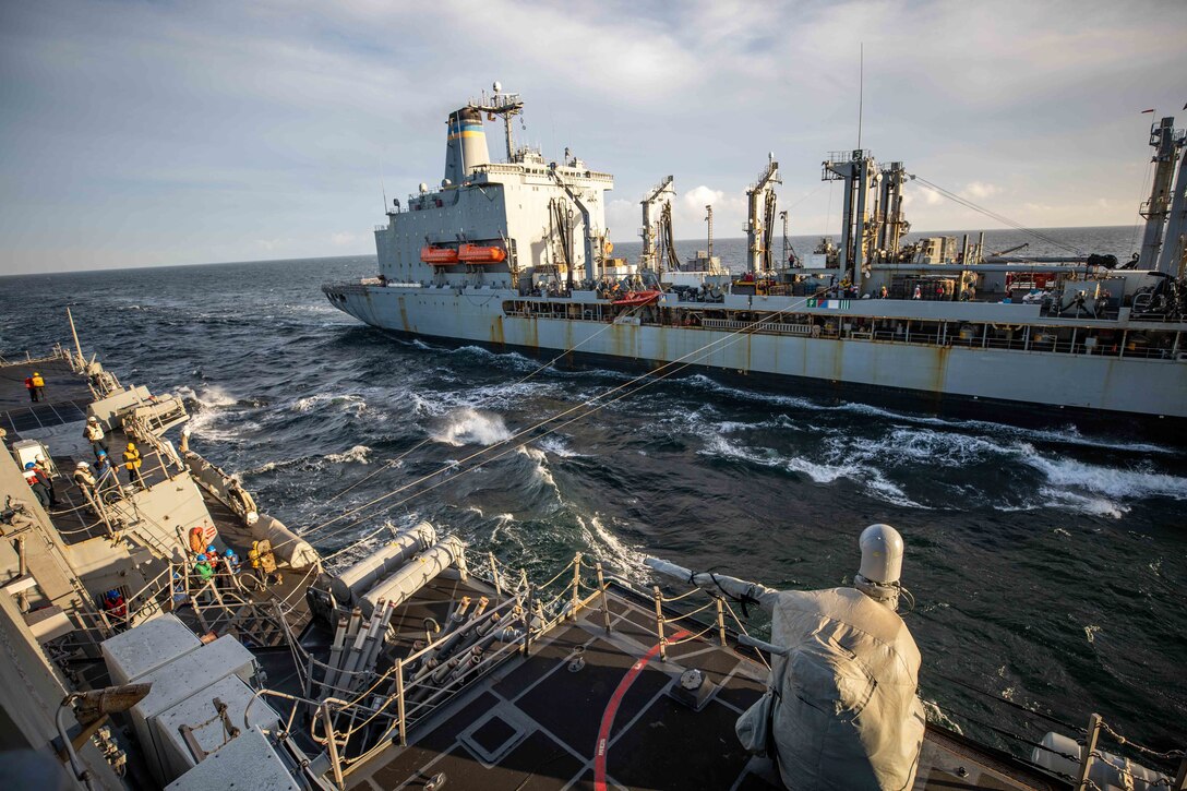 two Navy ships at sea with a fuel hose strung between them
