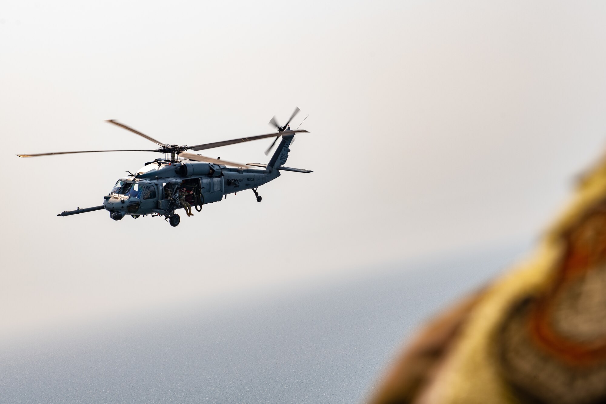 A U.S. Air Forces Pacific patch in the foreground is blurry while a helicopter flies in the background in focus.