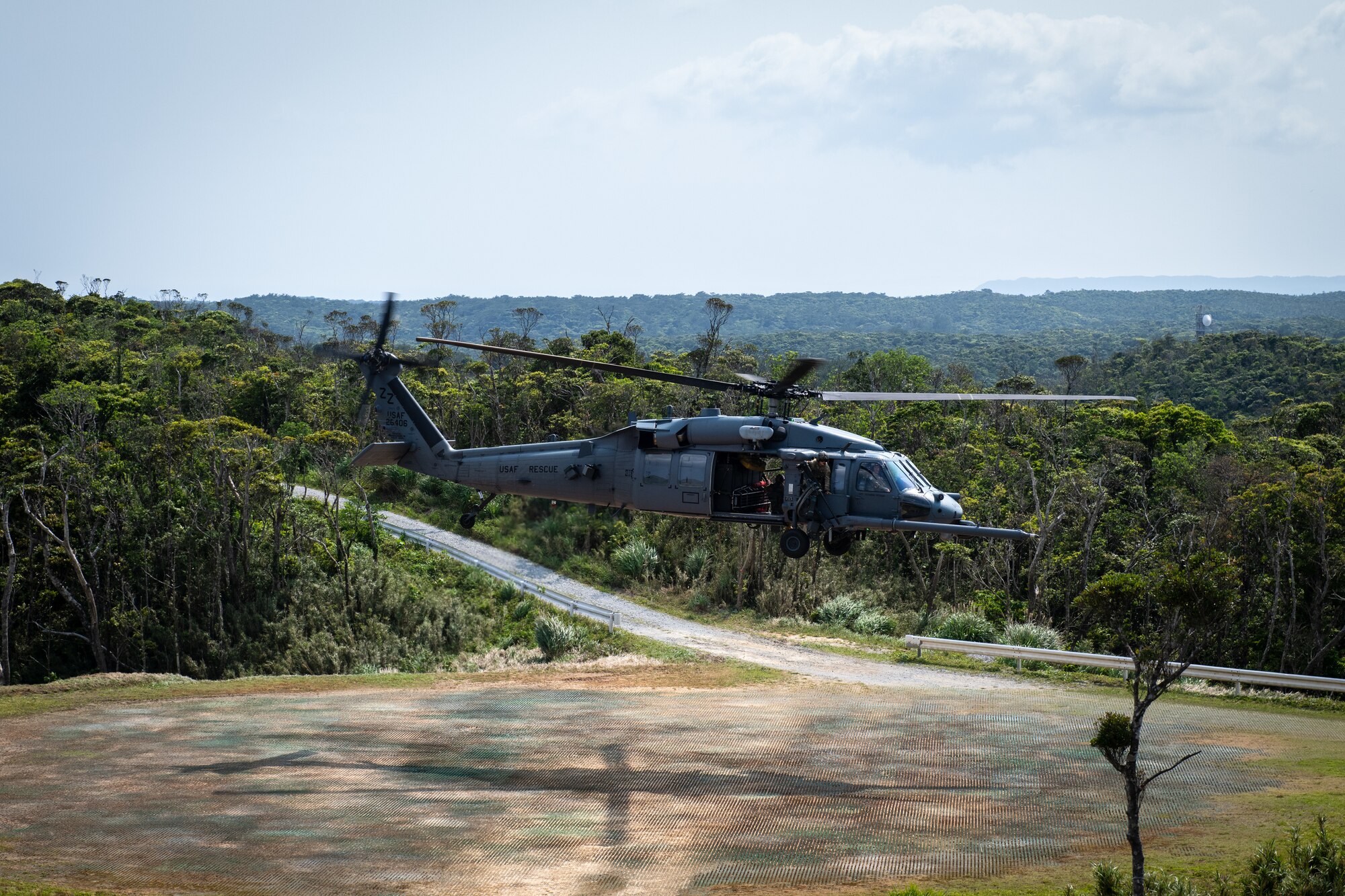A helicopter takes off from a landing pad in a wooded area.