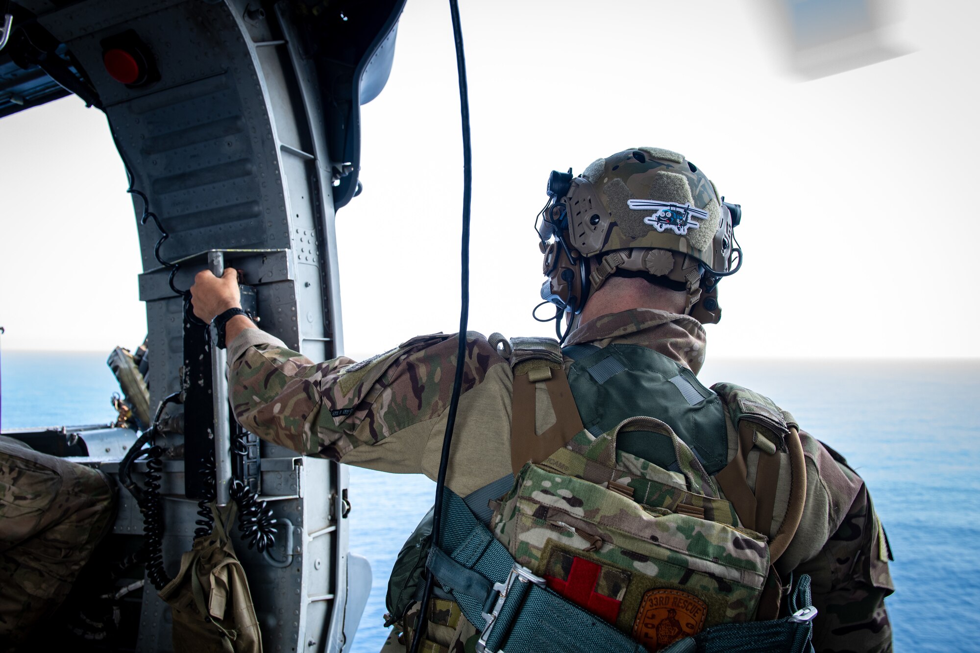 An Airman looks out over the ocean while flying in a helicopter.