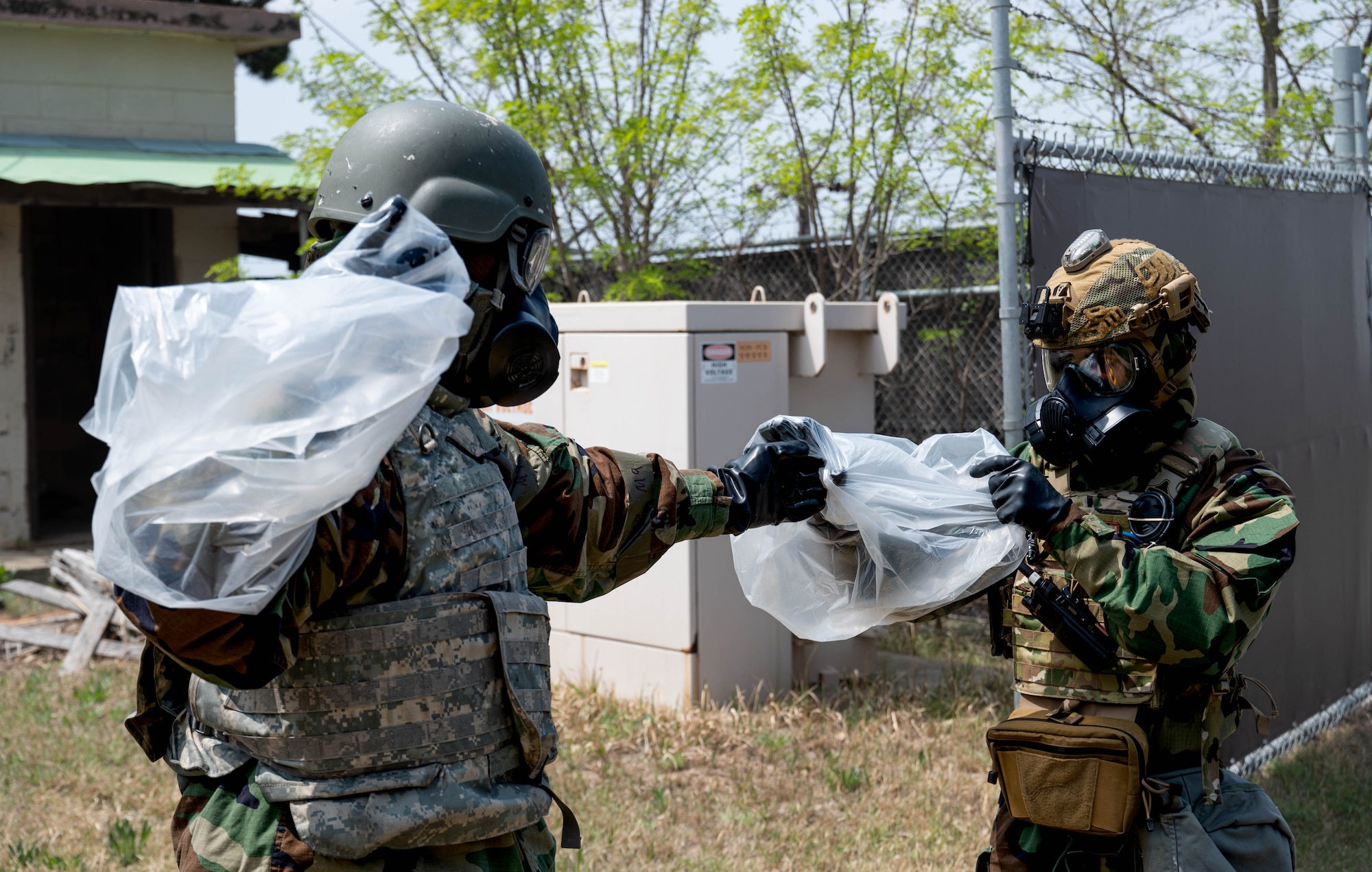 Senior Airman D’andre Goodson (right), 8th Civil Engineer Squadron explosive ordnance disposal technician, assists Airman 1st Class James Devlin (left), 8th CES EOD technician, with donning protective plastic coverings at Kunsan Air Base, Republic of Korea, April 20, 2023. The coverings provide extra protection to EOD members while they handle hazardous materials. (U.S. Air Force photo illustration by Senior Airman Shannon Braaten)