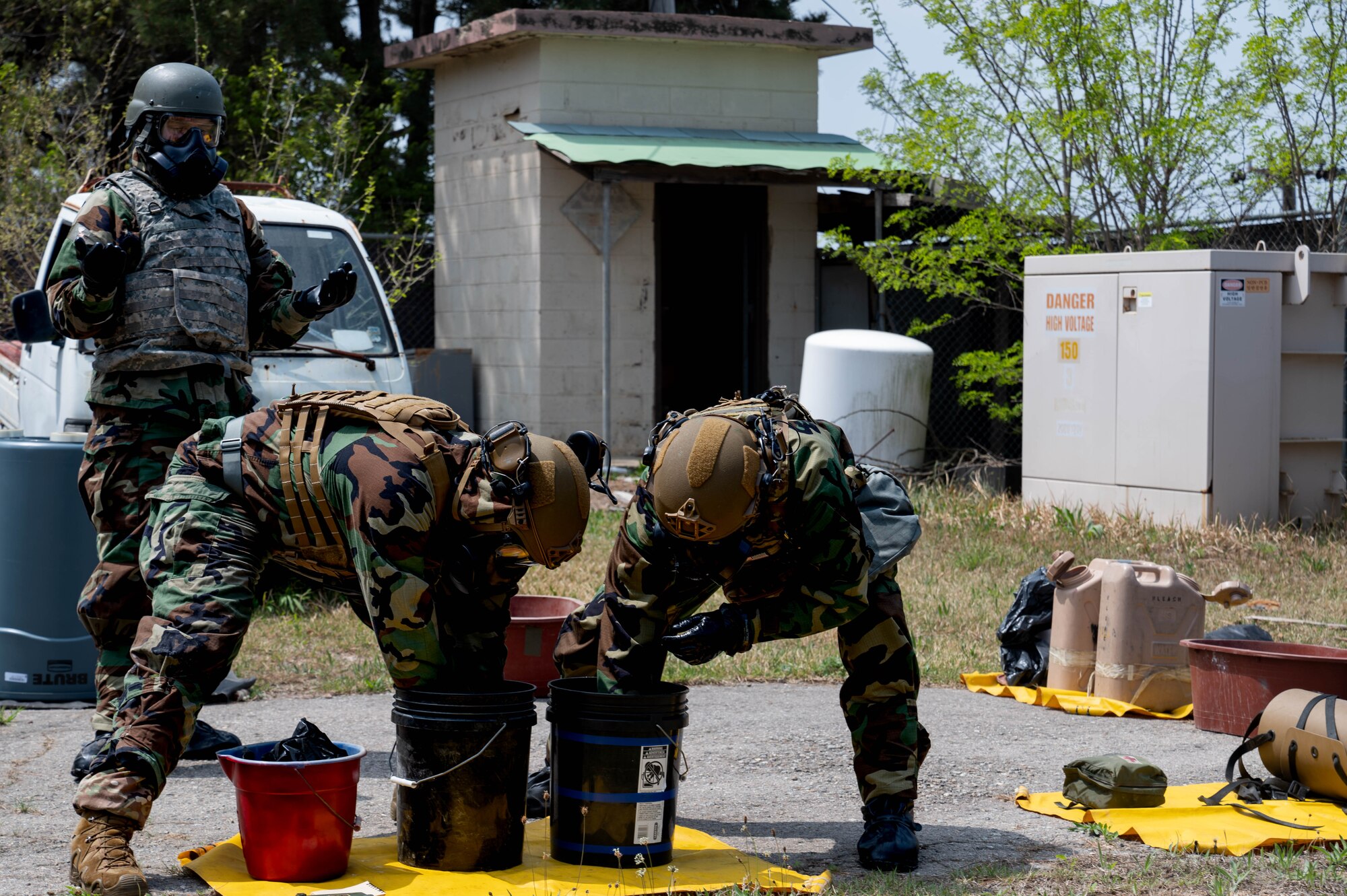 Explosive ordnance technicians from the 8th Civil Engineer Squadron, sanitize their Mission Oriented Protective Posture gear during a training event at Kunsan Air Base, Republic of Korea, April 20, 2023. The frequent sanitization of MOPP gear helps mitigate the risks associated with hazardous materials and limits the possibility of contamination outside the secure area. (U.S. Air Force photo illustration by Senior Airman Shannon Braaten)