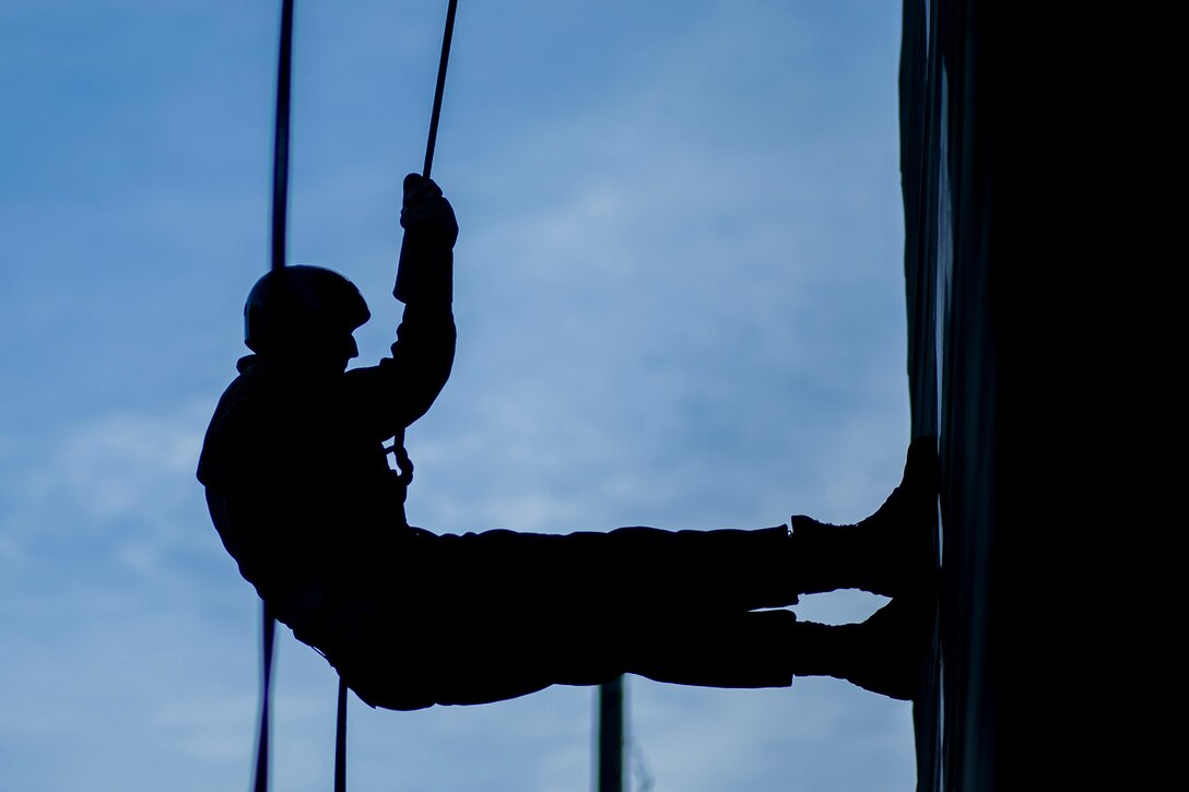 A Marine Corps recruit, shown in silhouette, rappels down a tower.