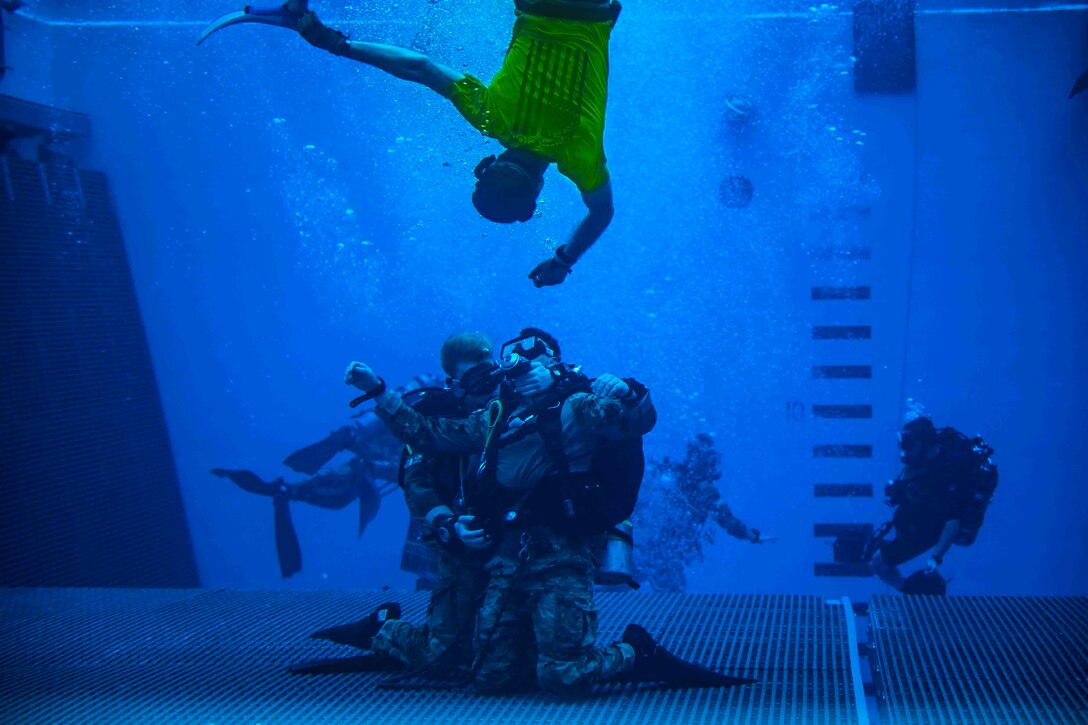 Airmen wearing dive gear move underwater in a pool.