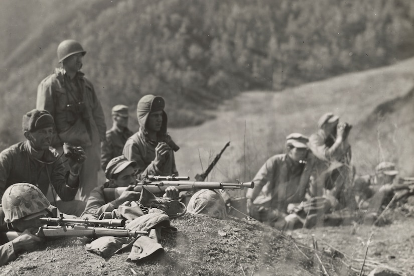 Men practice shooting rifles in the dirt.