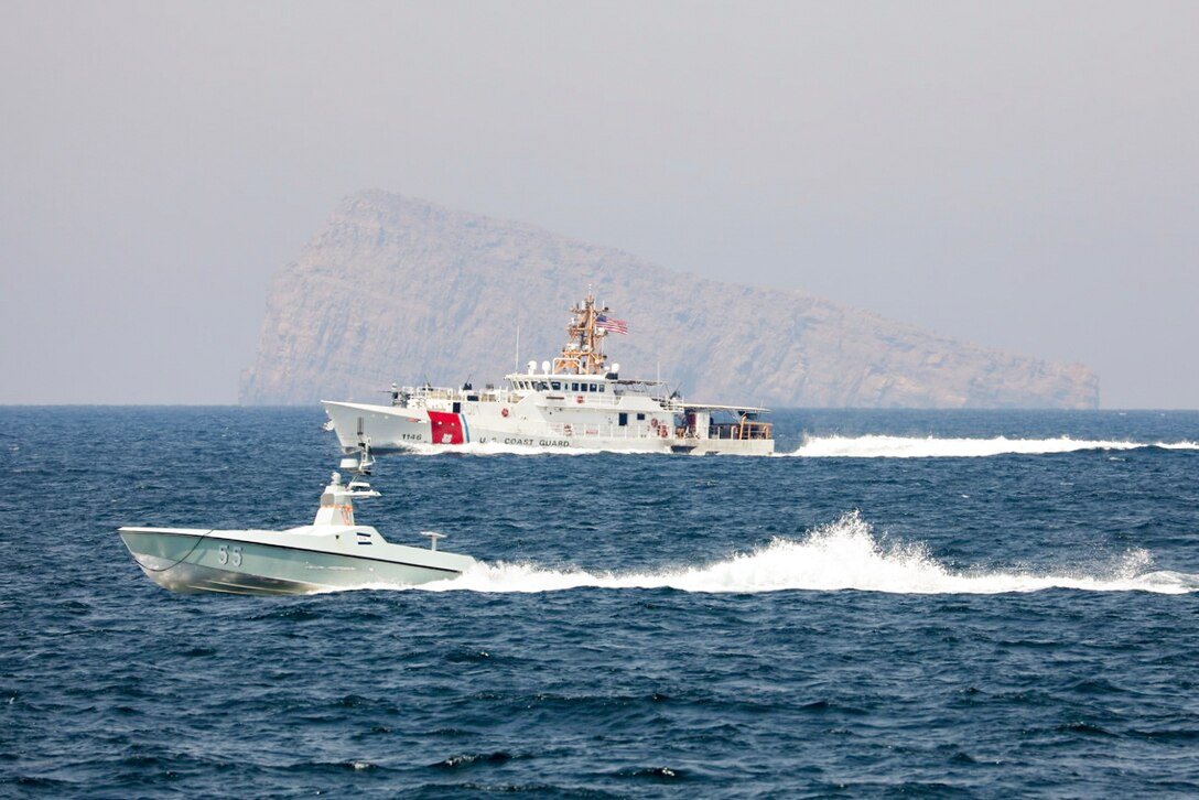 A ship and a small boat sail next to each other with a large rock in the background.