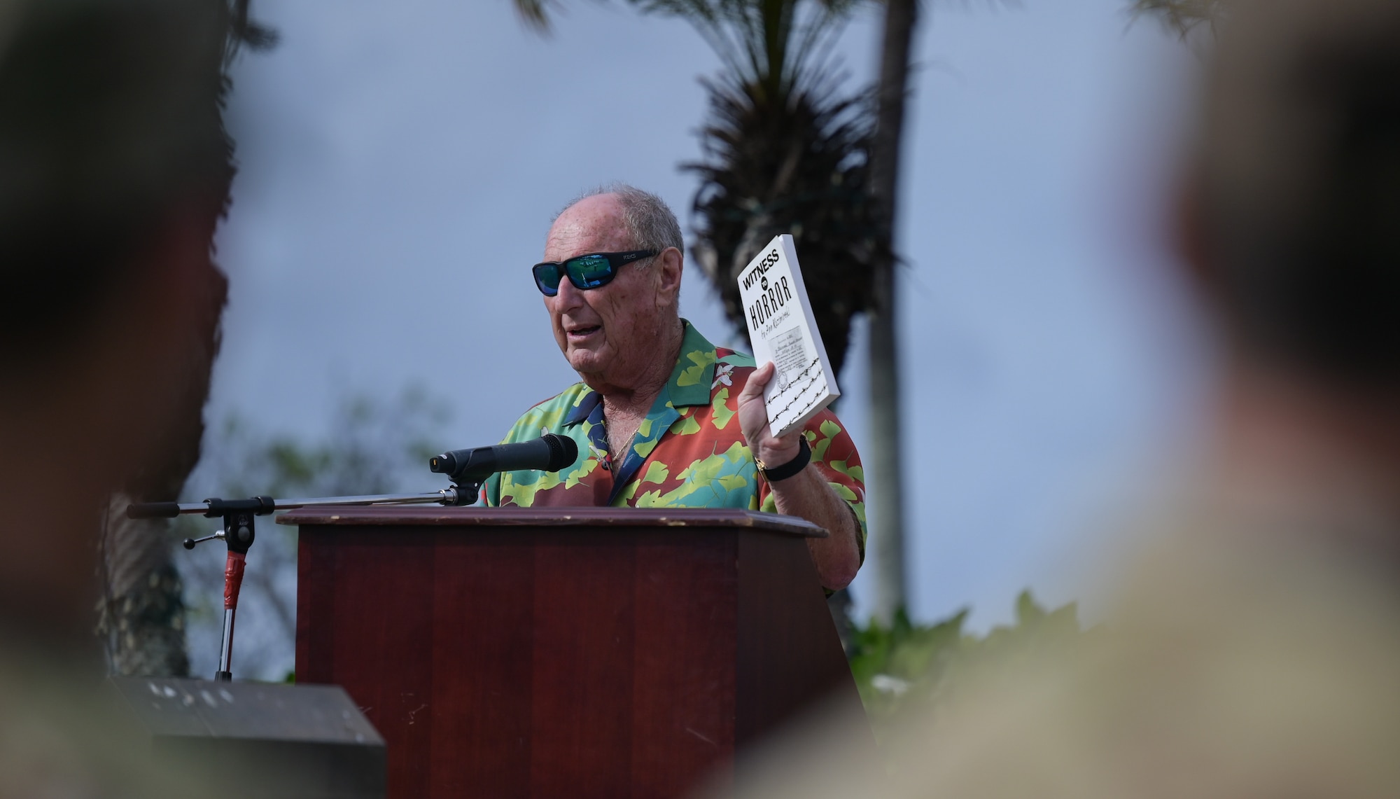 Seymour Kazimirski, the Holocaust Remembrance Ceremony keynote speaker, holds up a book written by his mother, a Holocaust survivor, during a Holocaust Remembrance Ceremony at the Missing Man Monument on Joint Base Pearl Harbor-Hickam, Hawaii, April 18, 2023. Kazimirski’s parents both escaped Nazi persecution during the Holocaust; he continues to share their stories and educate the local community. (U.S. Air Force photo by Staff Sgt. Alan Ricker)