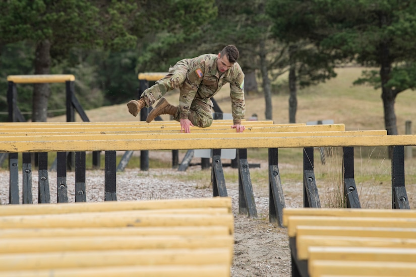 A man in military uniform propels his body over a beam.
