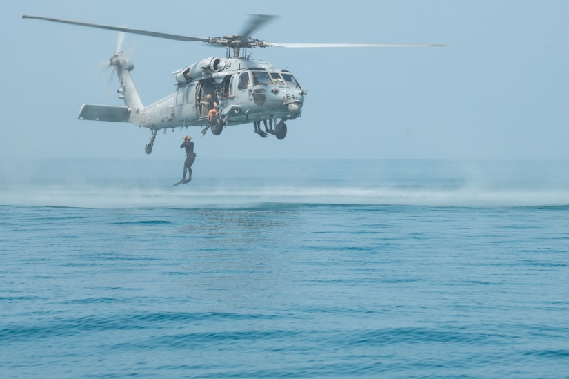 A man jumps from a helicopter into a body of water.