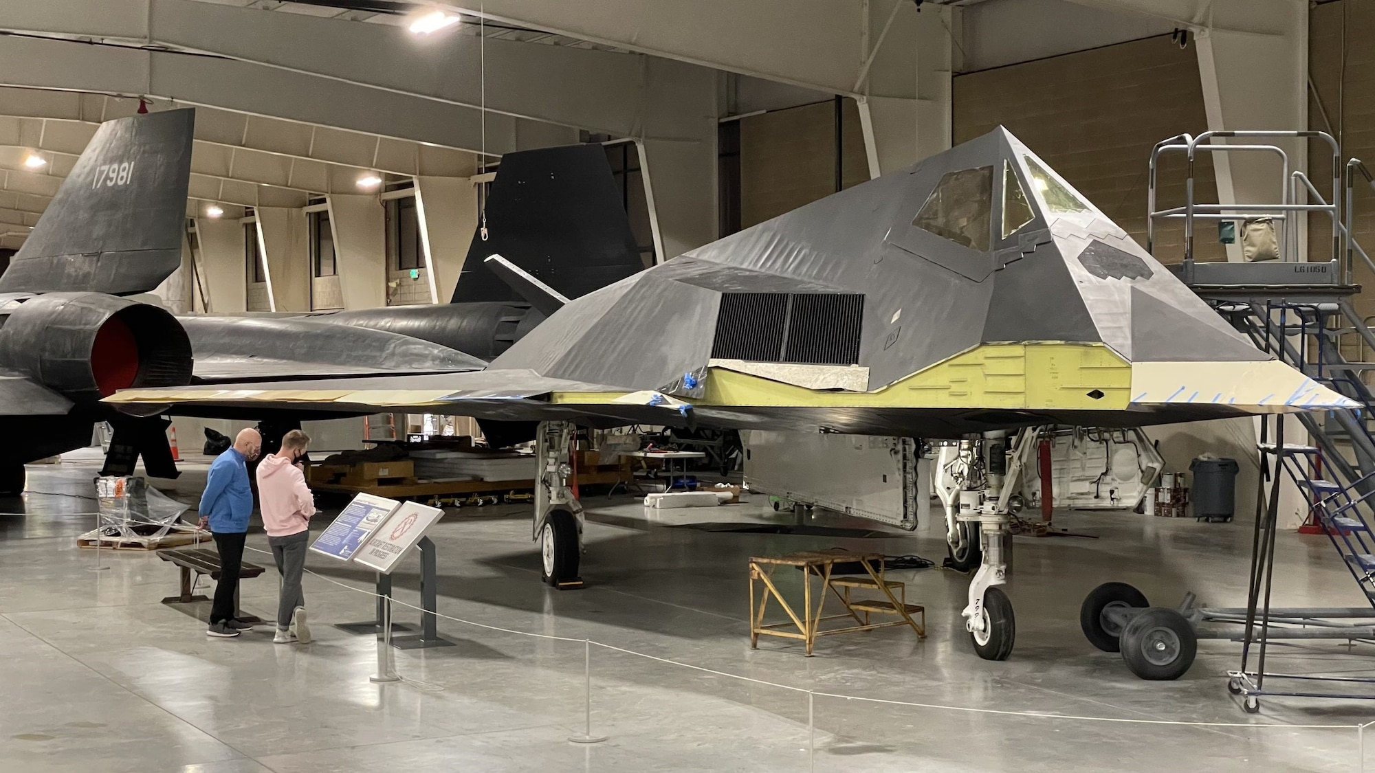 Two people looking at the F-117A without wings at Hill's Aerospace Museum