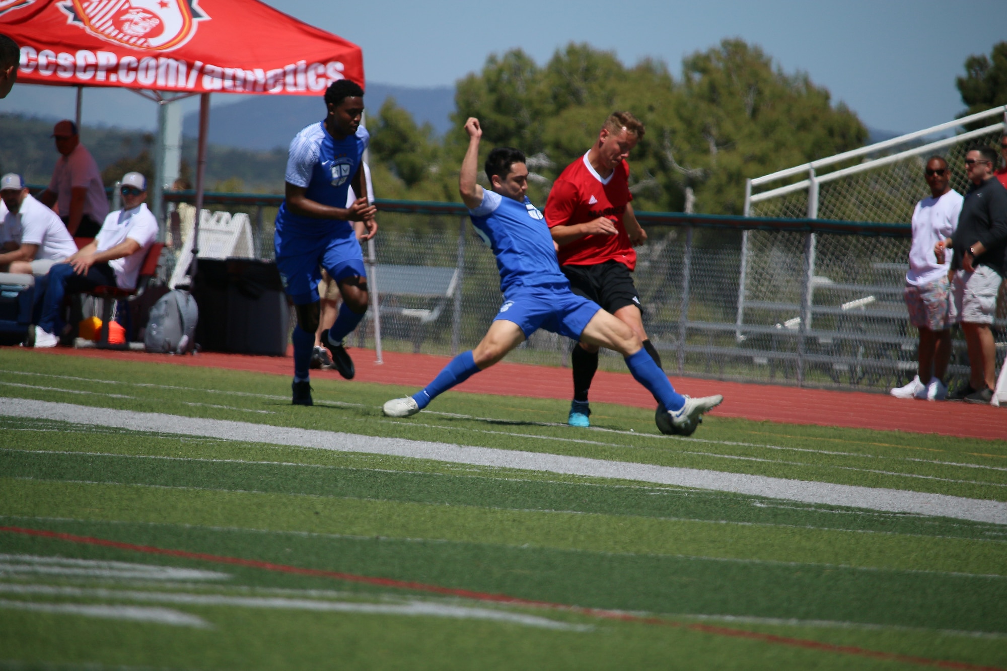 Two Air force players in blue go for a ball by a player in red.